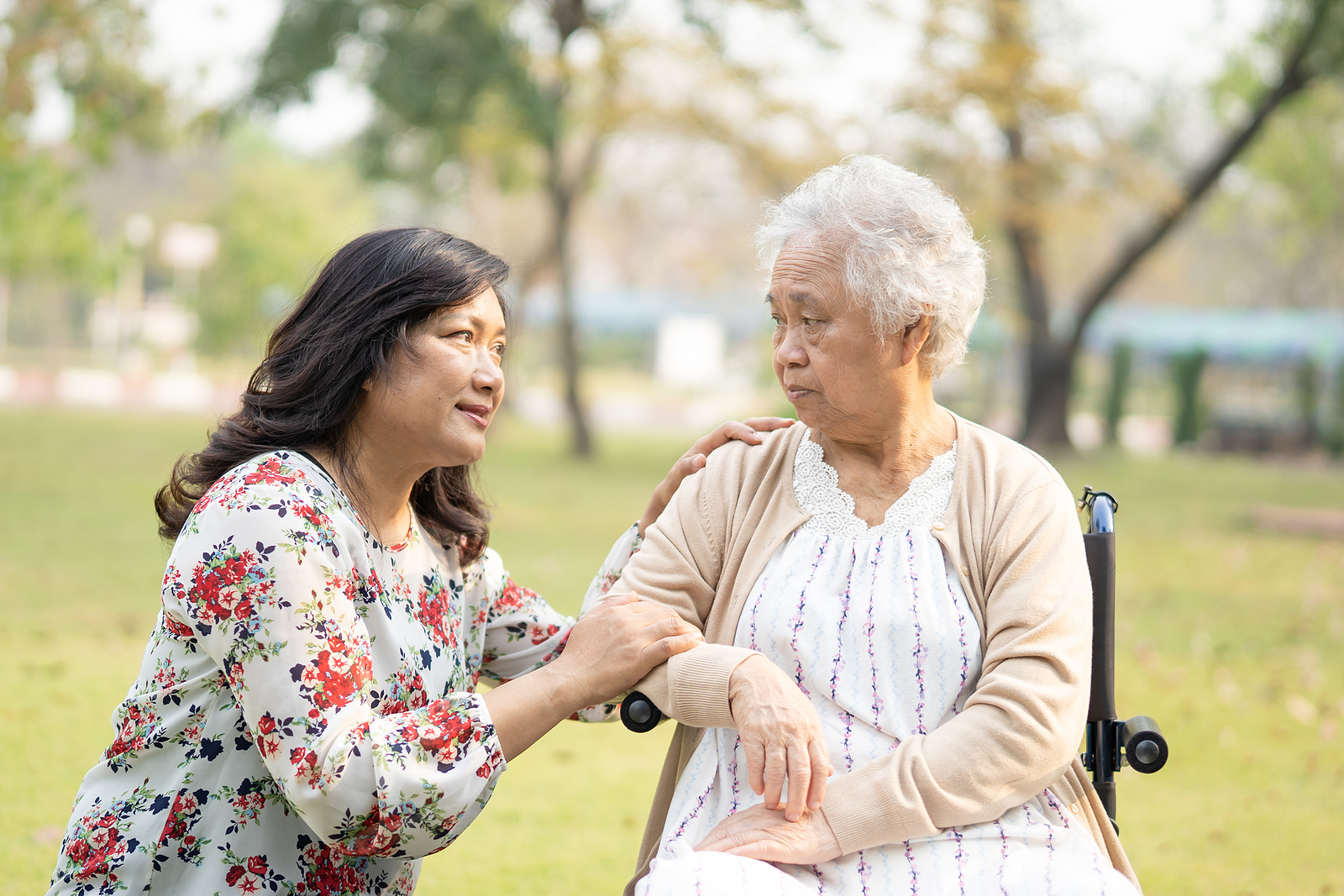 An elderly Asian woman is helped by a senior home care provider.