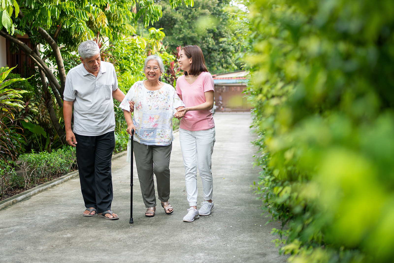 a senior woman using a cane to prevent falling as she walks along a path with family members