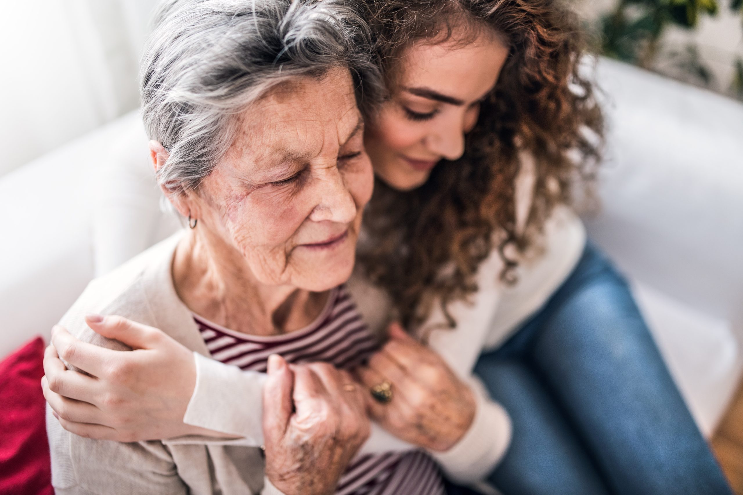 A daughter sits on the couch and hugs her aging mother after discussing home care options.