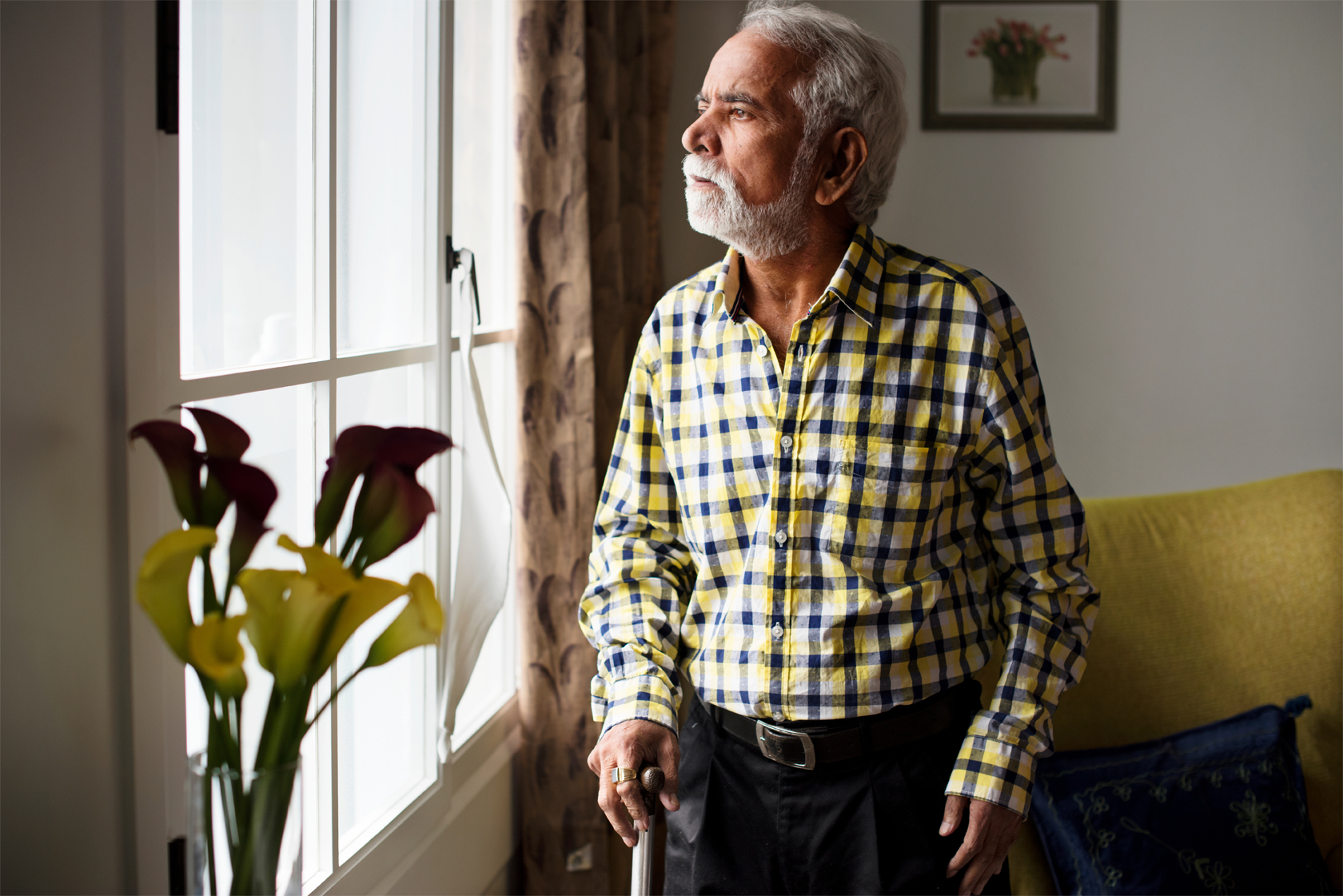 A senior man looks out the window of his home.