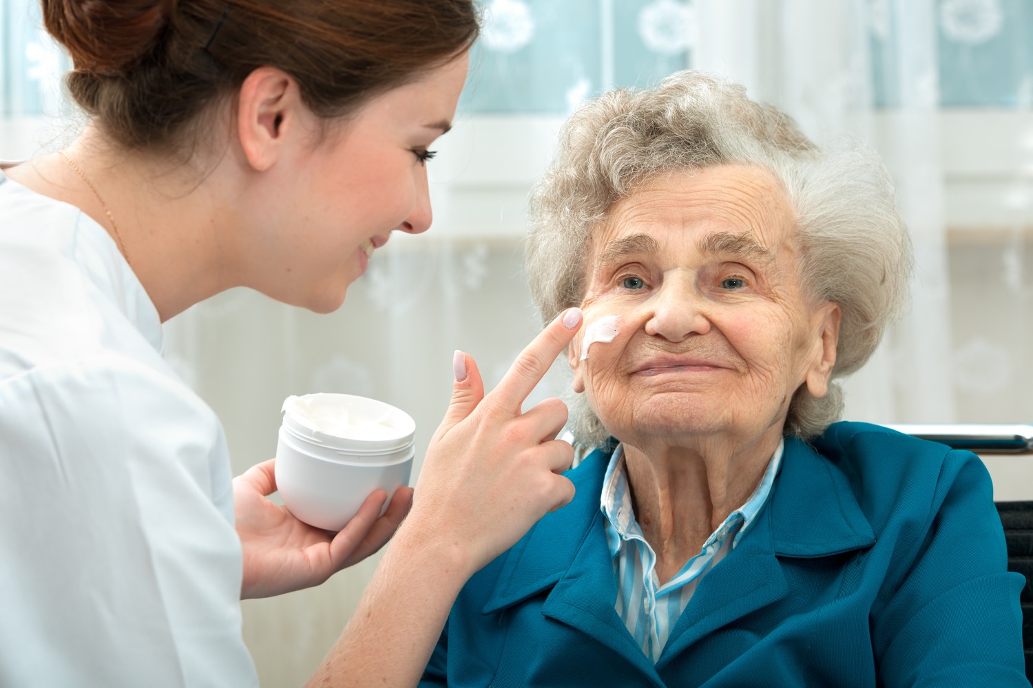 Caregiver applies facial cream to her client as part of the senior's personal care routine.