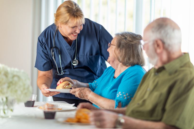 A live-in home care provider serves a senior couple breakfast.