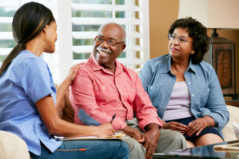 A live-in caregiver talks to a senior couple in their home.